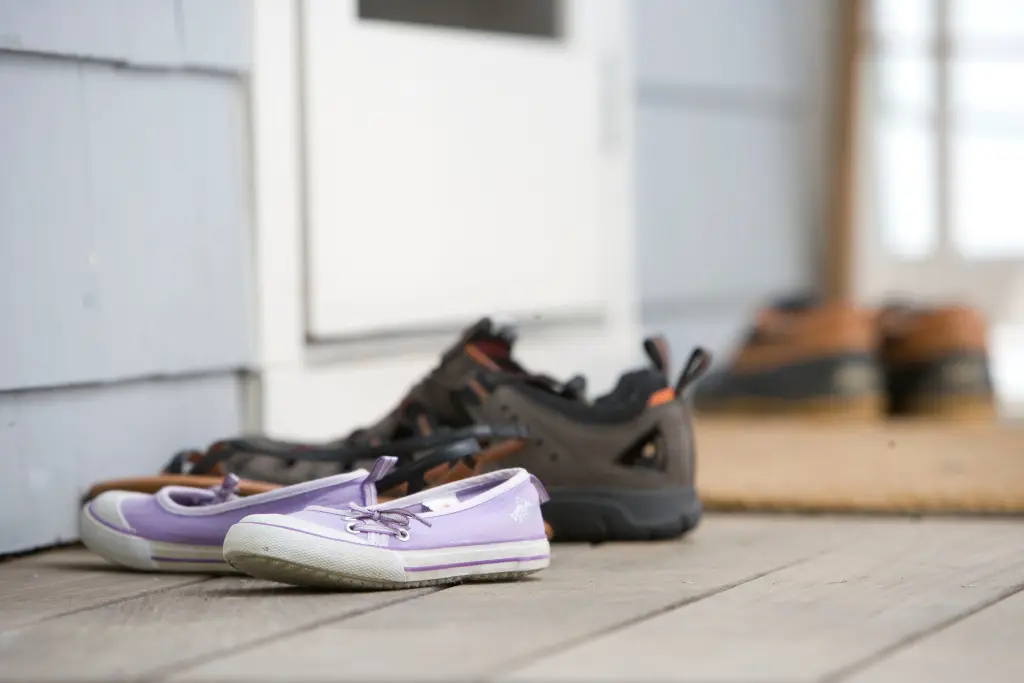 Three pairs of shoes - one lavender and white, one dark brown, and one a lighter brown and green, sitting on a porch.
